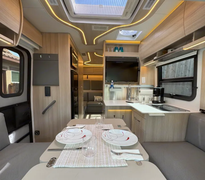This modern RV rental features a set dining table, compact kitchen, and a rear lounge, illuminated by unique ceiling lights.. Leisure Travel Vans Unity 2022