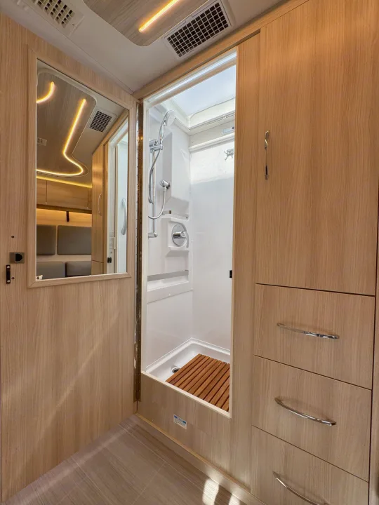 RV rental interior with a mirrored door, a well-appointed shower, and natural wood cabinetry.. Leisure Travel Vans Unity 2022