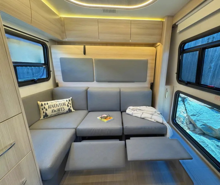 RV rental interior: A modern and inviting lounge with versatile grey sofa, pull-out footrests, overhead storage, and scenic windows.. Leisure Travel Vans Unity 2022