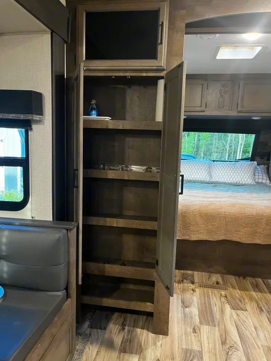View inside an **RV rental**: a tall pantry with open shelves, a bedroom, and part of the dining area.. Venture SPORTTREK 332VBH 2021