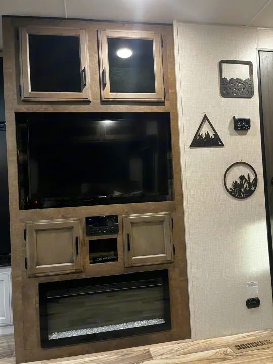 RV rental's cozy entertainment center: TV, electric fireplace, stereo, storage cabinets, and nature-themed wall decor.. Venture SPORTTREK 332VBH 2021