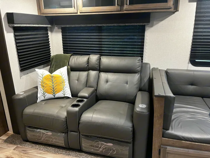 Inside an **rv rental**: plush grey reclining theater seats with cup holders and white stitching, under dark blinds.. Venture SPORTTREK 332VBH 2021