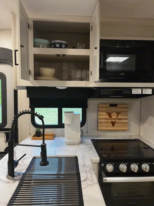 Modern RV rental kitchen featuring a microwave, oven, sink with drying rack, and coffee maker on marble-look countertops.. Venture SPORTTREK 332VBH 2021