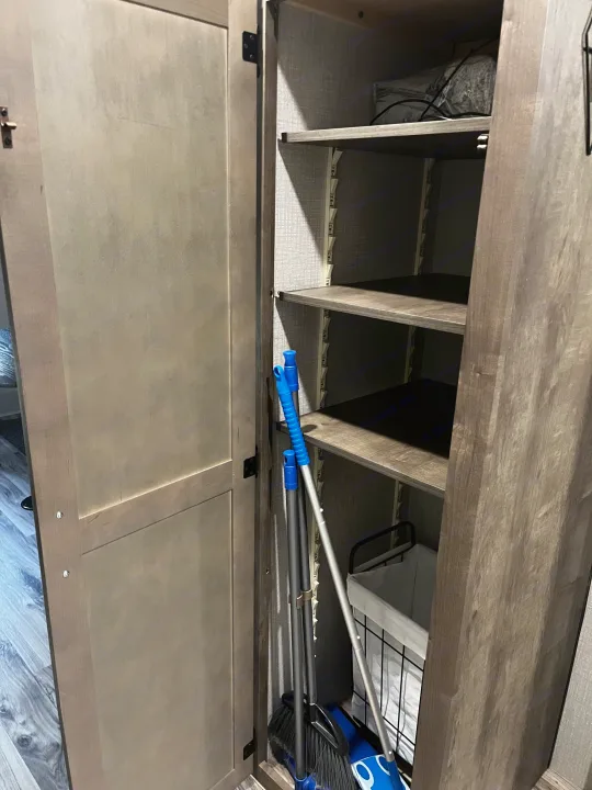 Practical RV rental storage: an open cabinet with shelves, housing a broom, dustpan, and hamper.. Venture SPORTTREK 332VBH 2021