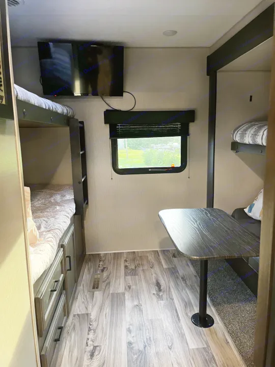Cozy RV rental interior featuring bunk beds with storage, a dining table, and a window with green views.. Venture SPORTTREK 332VBH 2021