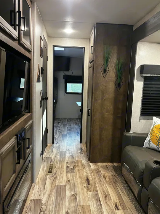 Modern RV rental interior showing living area, hallway, and bedroom view. Features wood-look floor, cabinets, and comfortable seating.. Venture SPORTTREK 332VBH 2021
