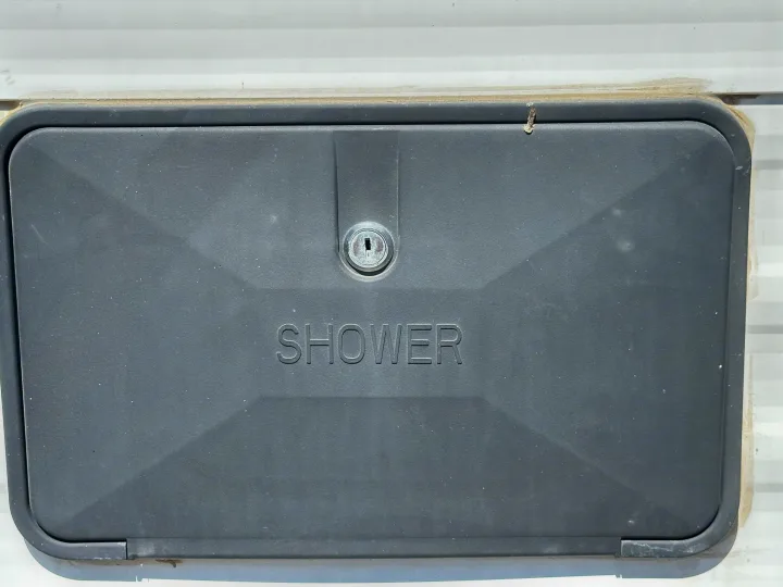 This grey exterior shower access panel on an RV rental features "SHOWER" embossed and a keyhole in the center.. Keystone RV Hideout 2020