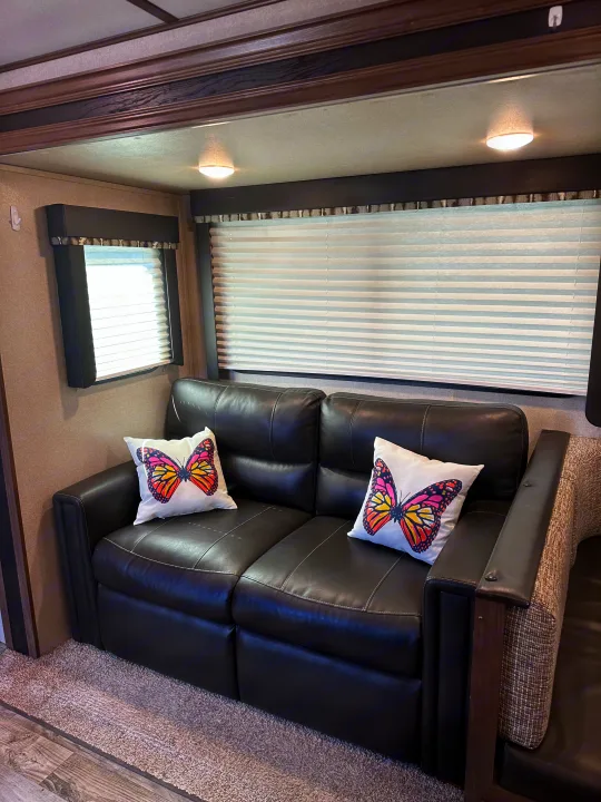 RV rental living space: dark leather sofa, bright butterfly pillows, and privacy blinds create a cozy feel.. Keystone RV Hideout 2020