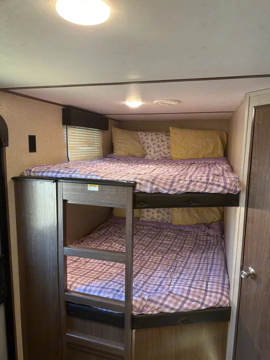 Cozy RV rental bunk beds, featuring purple checkered bedding and soft pillows. A compact sleeping area for travelers.. Keystone RV Hideout 2020