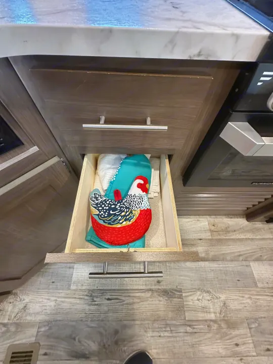 Open RV rental kitchen drawer revealing a playful chicken oven mitt and neatly folded towels.. Keystone RV Hideout 2020