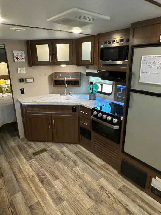 RV rental interior showcasing a modern kitchen with a sink, microwave, stove, and refrigerator. Features wood-grain flooring and dark wood cabinetry.. Keystone RV Hideout 2020
