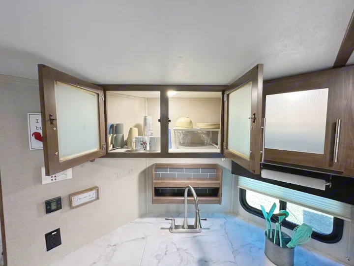 RV rental kitchen featuring open upper cabinets with dishes, a sink, marble countertop, and cooking utensils.. Keystone RV Hideout 2020