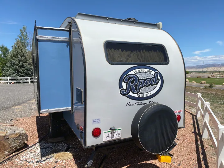 An Rpod travel trailer, an RV rental, with its side hatch open and spare tire, parked on gravel.. R-Pod Hood River Edition 2018