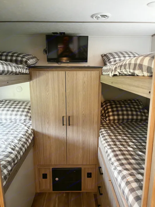 Explore this RV rental's bunk room! Four cozy beds with checkered bedding, TV, and storage for your adventure.. Keystone RV Passport SL 2021