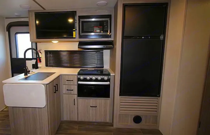 Well-equipped RV rental kitchen: sink, microwave, stove, fridge, TV, and ample storage.. Keystone RV Passport SL 2021