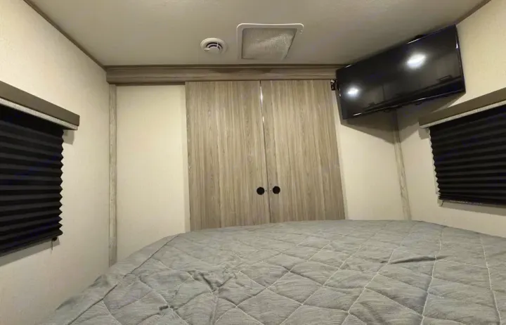 RV rental bedroom interior featuring a comfortable bed, mounted TV, closet doors, and window blinds. Cozy and functional space.. Keystone RV Passport SL 2021