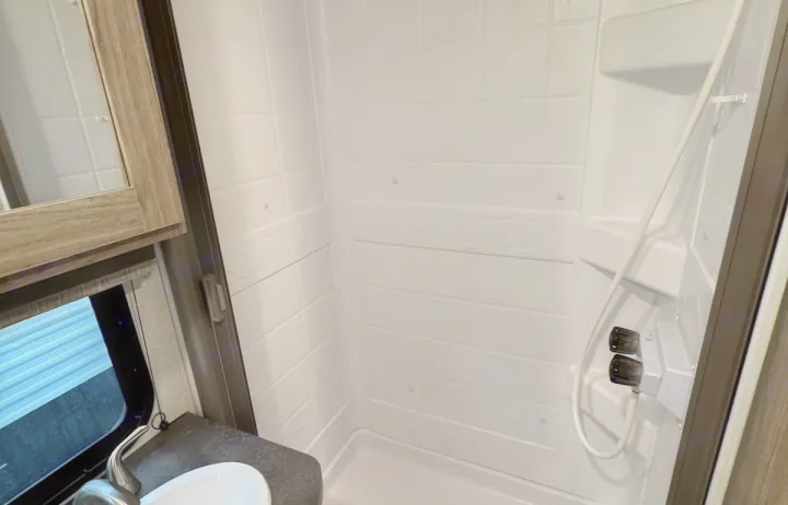 This RV rental features a bright, compact bathroom with a white shower stall, a small sink, and a mirrored cabinet.. Keystone RV Passport SL 2021