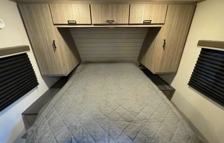 Spacious RV rental bedroom featuring a bed, ample overhead/side cabinets, and window blinds for privacy.. Keystone RV Passport SL 2021