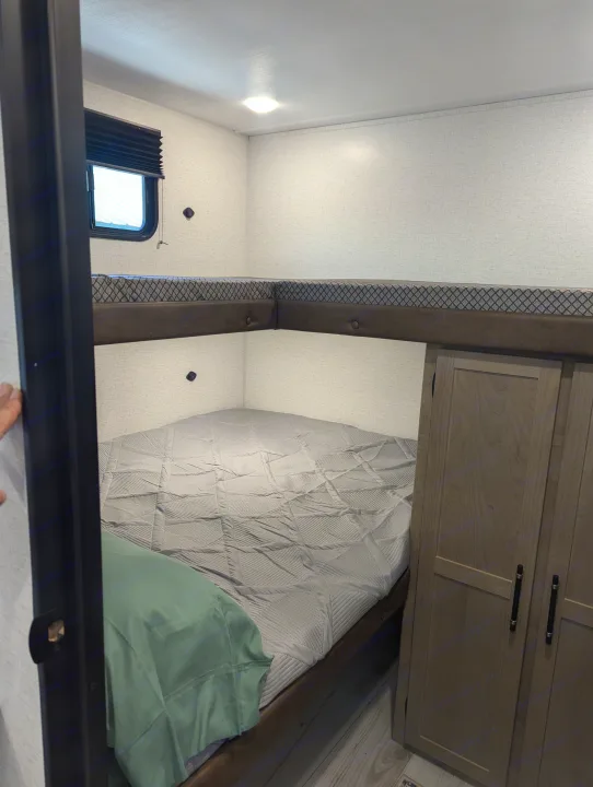 RV rental interior view: cozy bunk beds with a grey quilt, window, and wood wardrobe, designed for comfort.. Keystone Springdale Classic 291BRC 2025