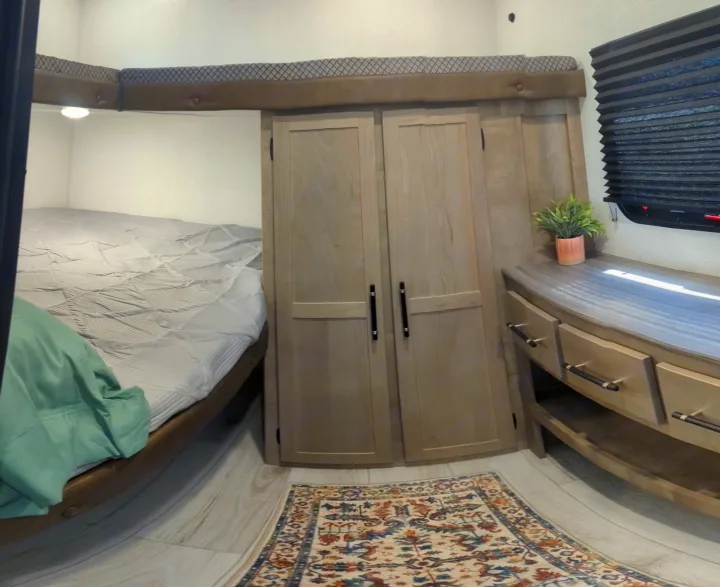 Modern RV rental interior featuring a bunk bed, wood wardrobe, dresser with plant, and a colorful rug.. Keystone Springdale Classic 291BRC 2025