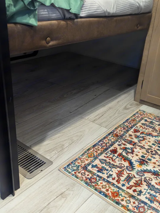 This rv rental features a cozy interior with a bed, light wood-look flooring, a colorful traditional rug, and a floor vent.. Keystone Springdale Classic 291BRC 2025
