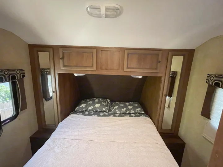 Inside an RV rental: a compact bedroom with a bed, animal-themed pillows, overhead cabinets, and side windows.. Cruiser RV Radiance 2015