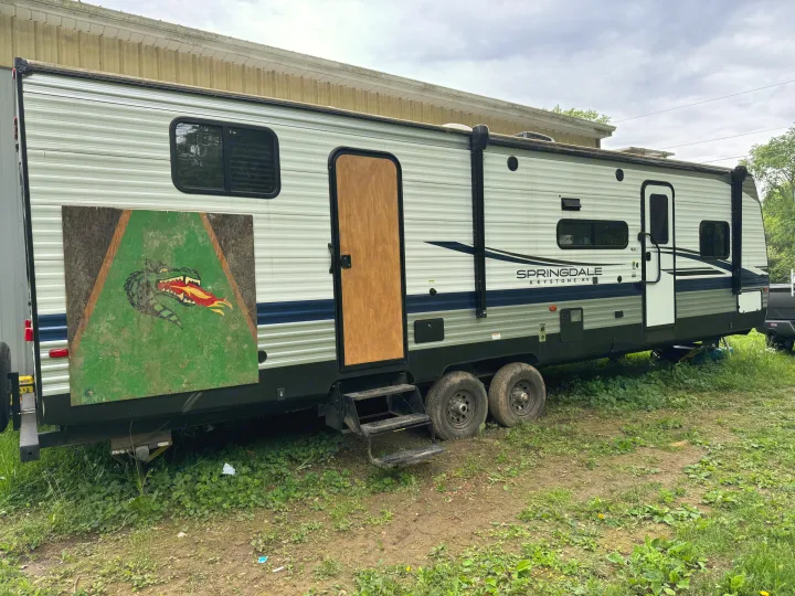 A Springdale Keystone travel trailer, ideal for an RV rental or camping, featuring a temporary wood door and a unique dragon art panel.. Keystone RV Springdale 2023