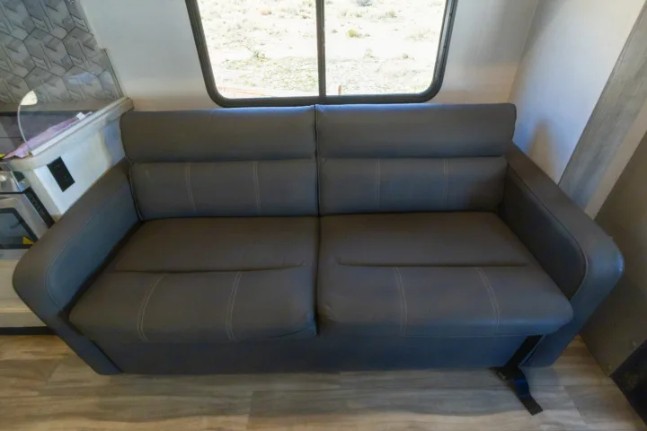Comfortable gray faux-leather sofa with seatbelts in an RV rental interior. Ideal for seating or converts to a bed.. Gulf Stream Conquest 2024