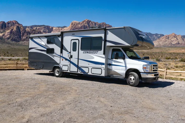 This rv rental, a sleek Conquest model, is parked on a gravel lot, framed by stunning desert mountains under a clear sky.. Gulf Stream Conquest 2024