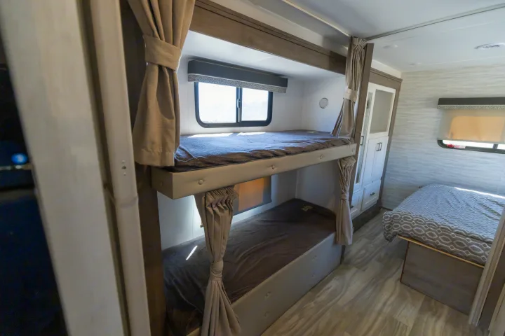 RV rental interior showing bunk beds with privacy curtains and a main bed, providing comfortable sleeping for travelers.. Gulf Stream Conquest 2024