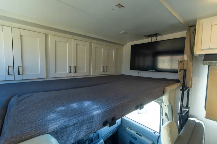 Spacious RV rental interior featuring a cab-over bunk bed, white cabinets, and TV, ideal for comfortable travel and sleeping.. Gulf Stream Conquest 2024