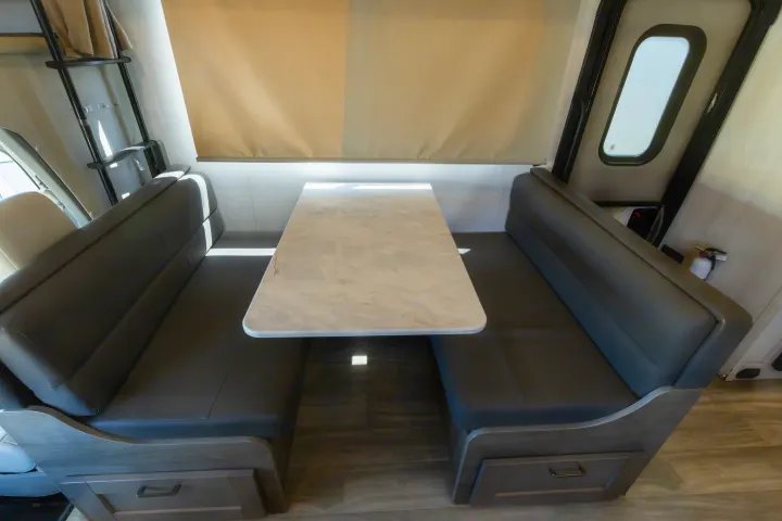 Modern RV rental dinette featuring dark gray booths, a marble-look table, and convenient under-seat storage.. Gulf Stream Conquest 2024