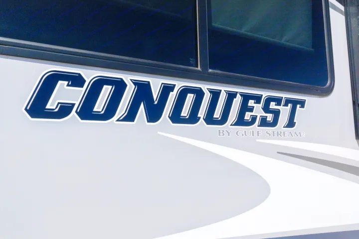 Close-up of a Conquest by Gulf Stream RV, with its distinctive blue and white branding on a grey body. Perfect for your RV rental.. Gulf Stream Conquest 2024