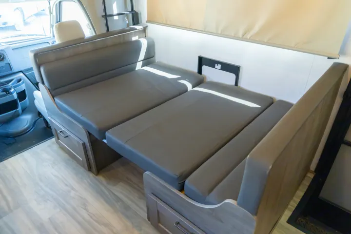 An RV rental features gray dinette seating converting to a bed, with wooden base cabinets & light floors.. Gulf Stream Conquest 2024