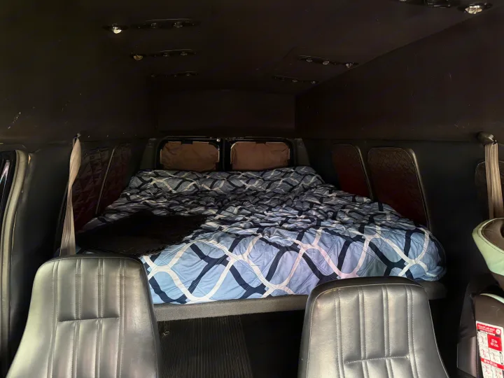 Cozy RV rental interior with a comfortable bed and front seating, ideal for mobile adventures and road trips.. Ford E350 Super Duty 1-ton Camper Van 2006