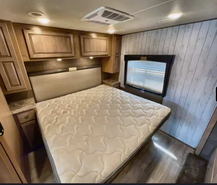 RV rental master bedroom showing a queen bed, light wood cabinets, and bright interior lighting.. Thor Windsport 2019