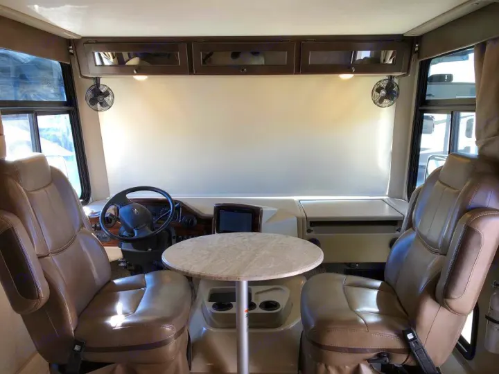 Spacious RV rental cockpit with swiveling leather captain's chairs, steering wheel, and a center table, ideal for travel.. Thor Windsport 2019