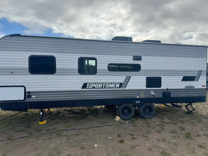 This gray KZ Sportsmen travel trailer, an RV rental, is parked at a campsite, ready for adventure under a cloudy sky.. KZ Sportsmen SE 260BHSE 2022