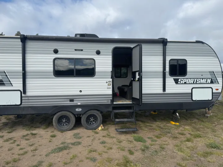 Grey travel trailer RV rental parked on dirt with open door, ready for camping adventures.. KZ Sportsmen SE 260BHSE 2022