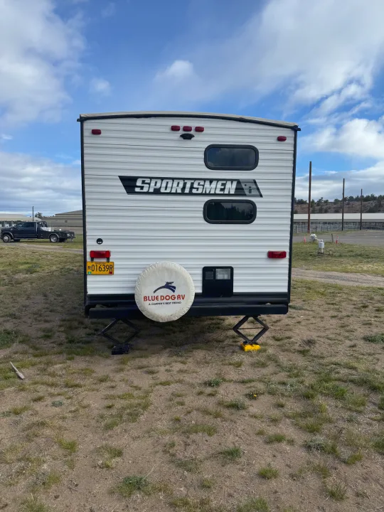 Rear of a white Sportsmen travel trailer, great for rv rental. Features Oregon plate, Blue Dog RV cover, & deployed stabilizer jacks.. KZ Sportsmen SE 260BHSE 2022