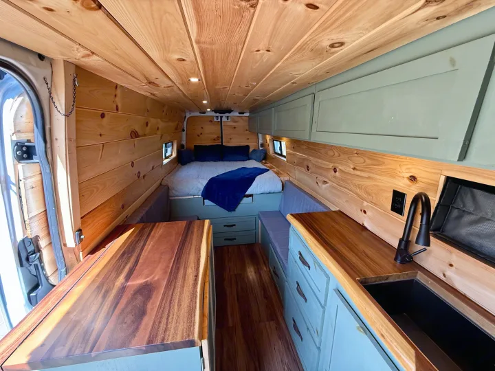 This custom RV rental interior features warm wood paneling, a cozy bed, and a well-equipped kitchen.. Dodge Sprinter 3500 2007