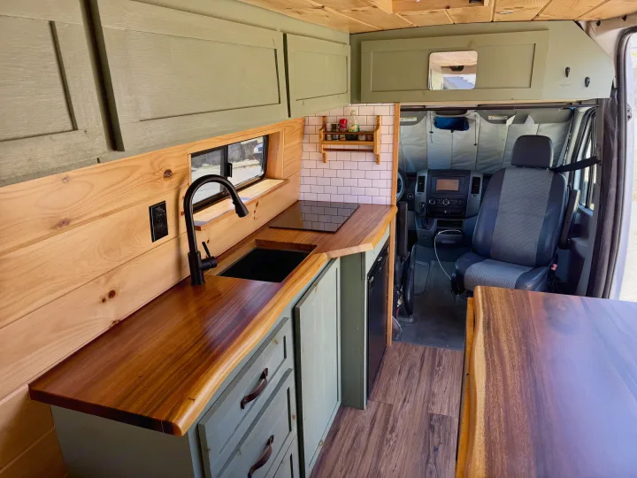 Inside this modern RV rental: a well-equipped camper van kitchen with wood counters, sink, cooktop, and stylish storage.. Dodge Sprinter 3500 2007