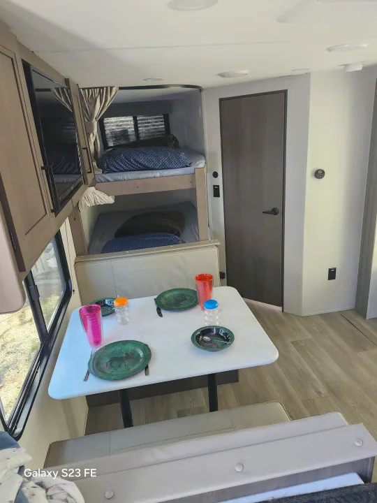 Cozy RV rental interior with a dining table, comfy bench seats, and bunk beds in the background for compact living.. Grand Design Transcend 2025