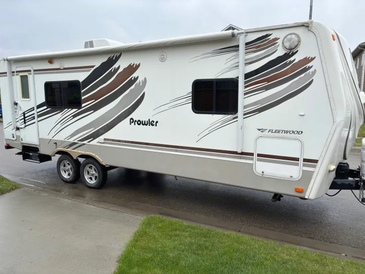 White and brown Fleetwood Prowler travel trailer, ideal for an RV rental, parked on a wet street.. Fleetwood 230RKS 2009