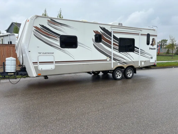 A white Fleetwood Prowler travel trailer, an excellent RV rental option, parked on a wet street.. Fleetwood 230RKS 2009