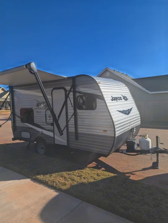 A white Jayco travel trailer, an ideal RV rental, parked with its awning extended under a clear blue sky.. Jayco Jay Flight SLX 2021
