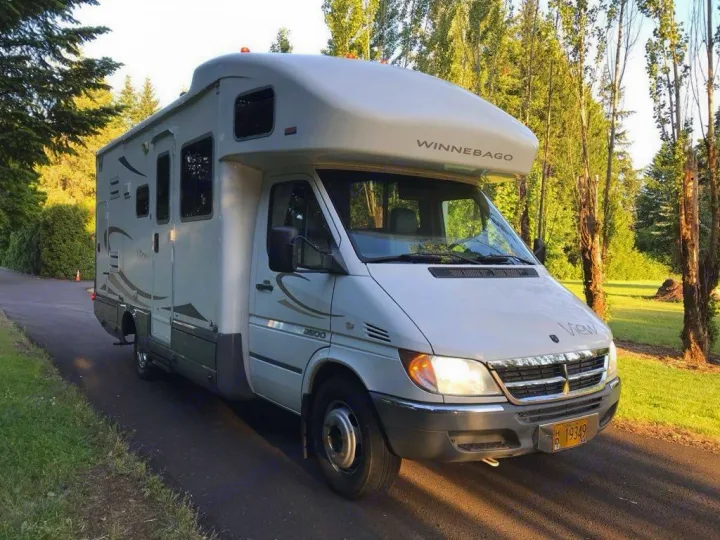 Winnebago View motorhome, a white RV rental, parked on a drive with trees & grass. Ideal for your next road trip.. Winnebago View 2006