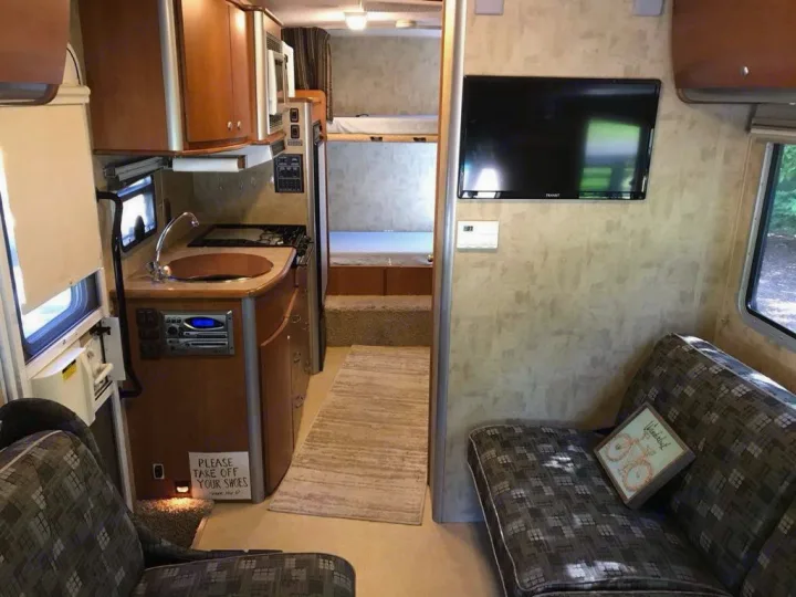 Clean rv rental interior featuring a kitchen, living area with TV, and sleeping berths. Note the 'please take off your shoes' sign.. Winnebago View 2006