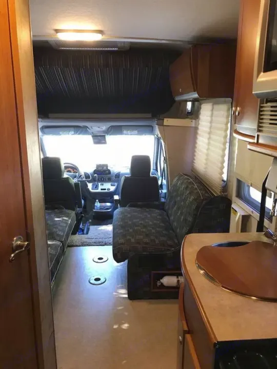 Inside a bright RV rental, showcasing the cockpit, lounge seating, and a compact kitchen area.. Winnebago View 2006