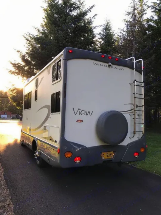 A white and gray Winnebago View RV, seen from the rear, parked on pavement with trees. Plan your next rv rental adventure!. Winnebago View 2006